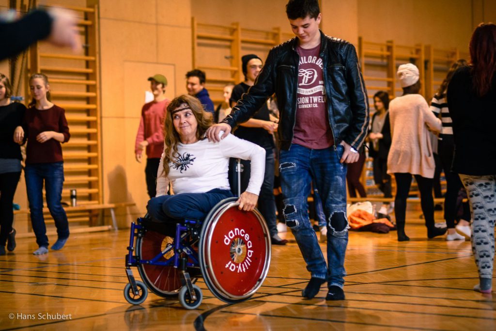 Ein Jugendliche lässt sich von einer Künstlerin im Rollstuhl mit verschlossenen Augen führen.