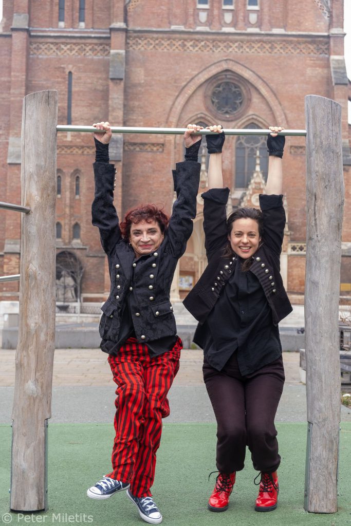 Die zwei Künstlerinnen sind rot-schwarz gekleidet und hängen glücklich nebeneinander an einer Stange herum.